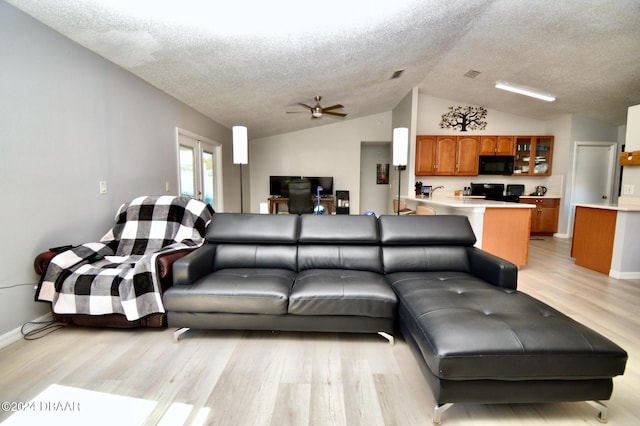 living room featuring lofted ceiling, a textured ceiling, light hardwood / wood-style flooring, and ceiling fan