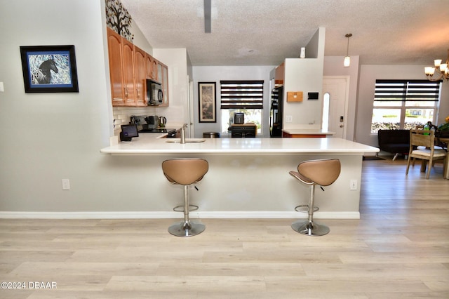 kitchen with decorative light fixtures, light hardwood / wood-style flooring, a kitchen breakfast bar, kitchen peninsula, and black appliances