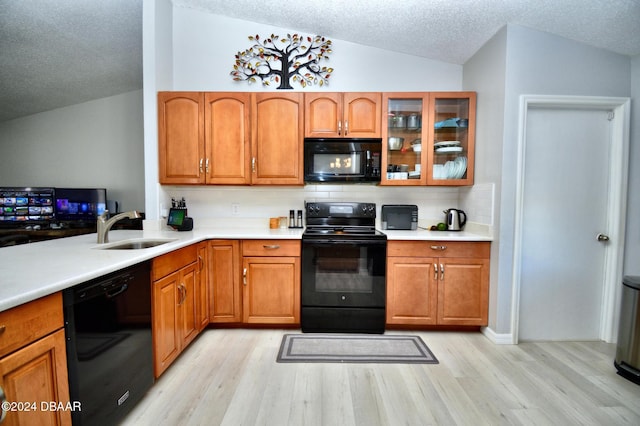 kitchen with light wood-type flooring, lofted ceiling, sink, and black appliances