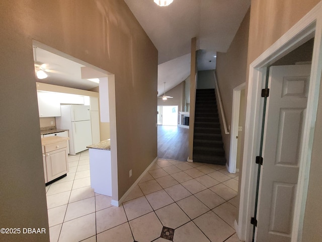 hallway with light tile patterned floors, stairway, lofted ceiling, and baseboards