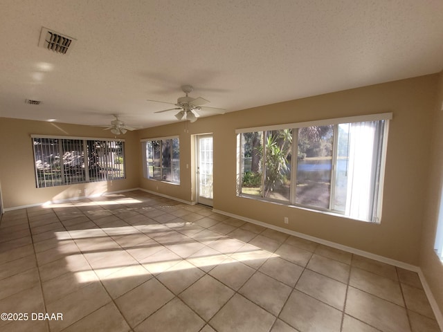 tiled empty room with a textured ceiling, visible vents, and baseboards