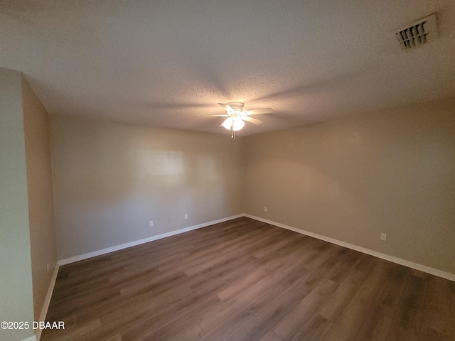 empty room featuring dark wood-style floors, visible vents, a ceiling fan, a textured ceiling, and baseboards