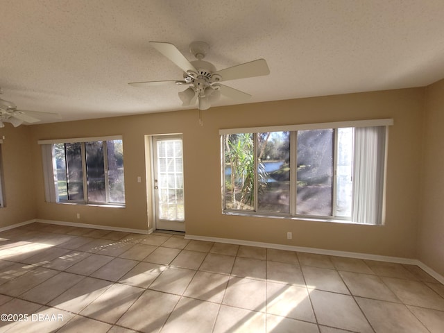 tiled empty room featuring a healthy amount of sunlight, ceiling fan, baseboards, and a textured ceiling