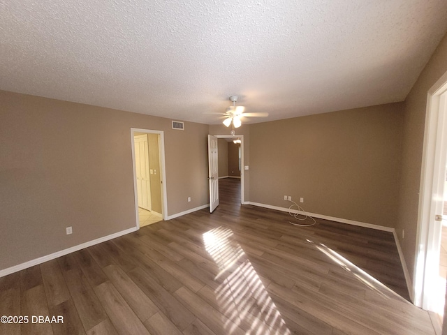 spare room with a textured ceiling, wood finished floors, a ceiling fan, visible vents, and baseboards