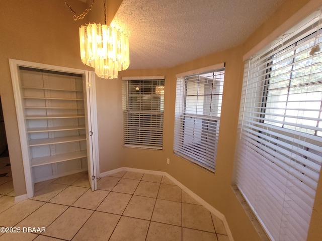 unfurnished dining area featuring tile patterned flooring, a notable chandelier, a textured ceiling, and baseboards