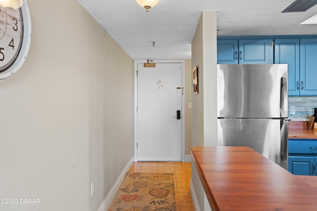 kitchen with blue cabinetry, butcher block counters, stainless steel fridge, and light tile patterned floors