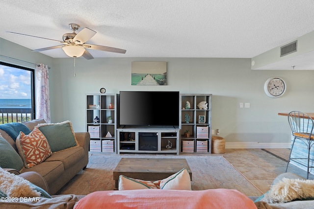 living room with a textured ceiling, a water view, ceiling fan, and light tile patterned flooring