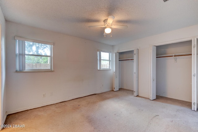 unfurnished bedroom featuring two closets, light colored carpet, ceiling fan, and a textured ceiling