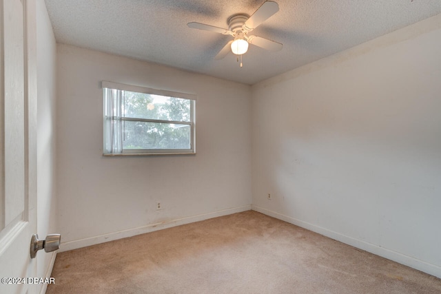 spare room with a textured ceiling, light colored carpet, and ceiling fan