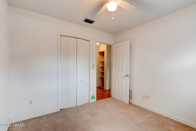 unfurnished bedroom with light colored carpet, a textured ceiling, ceiling fan, and a closet