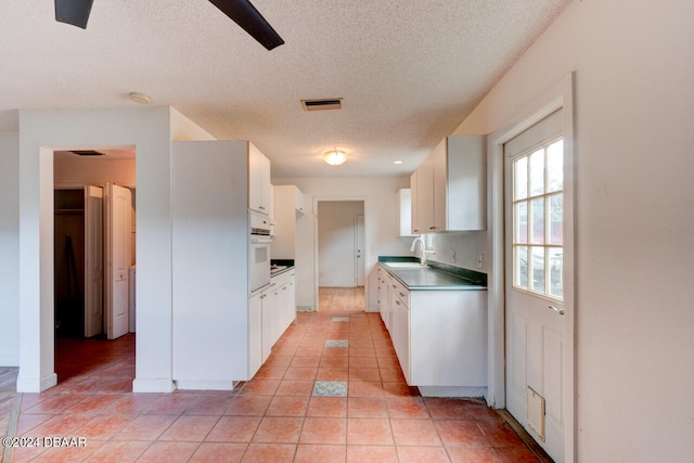 kitchen with sink, white oven, a textured ceiling, light tile patterned flooring, and white cabinets