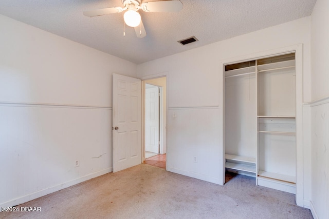 unfurnished bedroom with a textured ceiling, light colored carpet, a closet, and ceiling fan