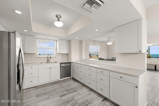 kitchen with appliances with stainless steel finishes, sink, white cabinets, kitchen peninsula, and a raised ceiling