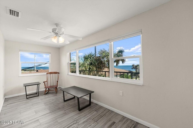 sitting room with light wood-type flooring, ceiling fan, and a water view