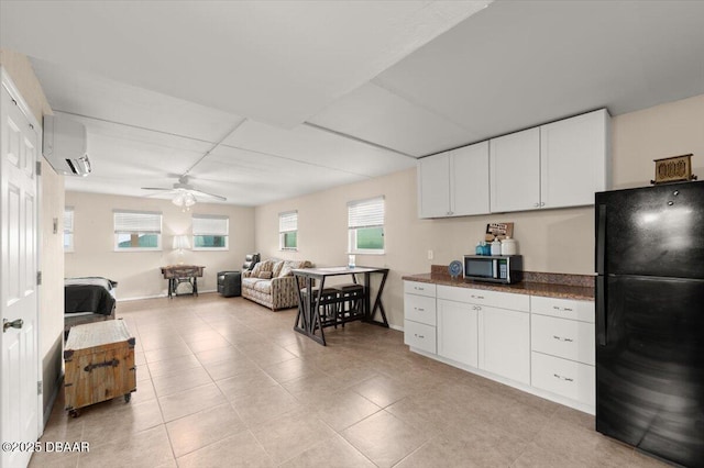 kitchen with light tile patterned floors, ceiling fan, a wall unit AC, white cabinets, and black fridge