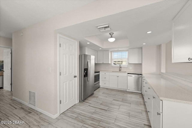 kitchen featuring white cabinetry, sink, a raised ceiling, and appliances with stainless steel finishes