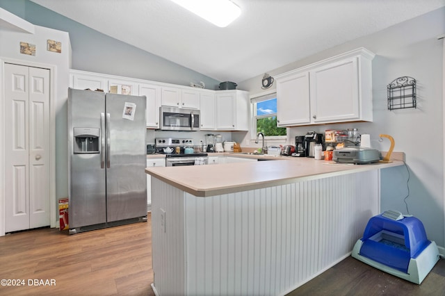 kitchen with stainless steel appliances, kitchen peninsula, wood-type flooring, lofted ceiling, and white cabinets