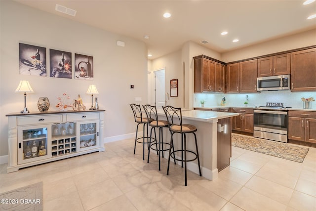 kitchen featuring stainless steel appliances, backsplash, light tile patterned floors, a breakfast bar, and a center island