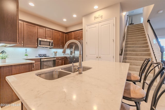 kitchen with light stone counters, decorative backsplash, sink, a breakfast bar, and appliances with stainless steel finishes