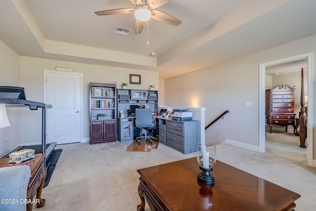 carpeted home office with ceiling fan and a raised ceiling