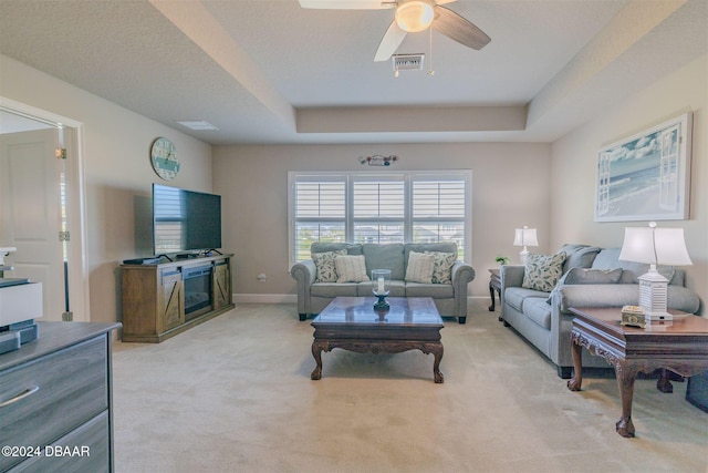 carpeted living room with ceiling fan and a raised ceiling