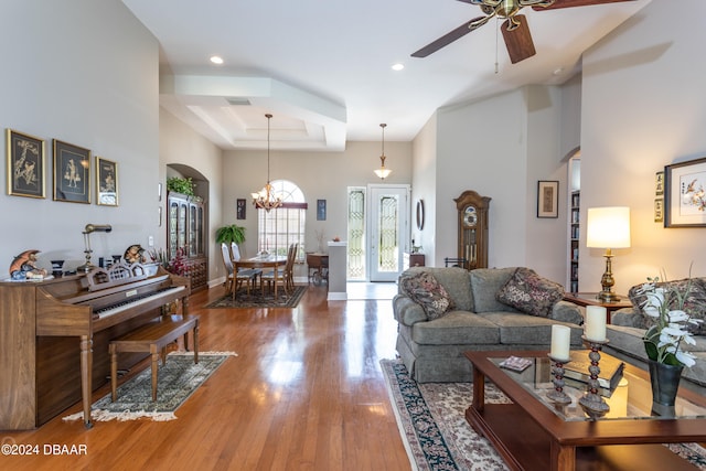 living room with a high ceiling, a tray ceiling, hardwood / wood-style flooring, and ceiling fan with notable chandelier