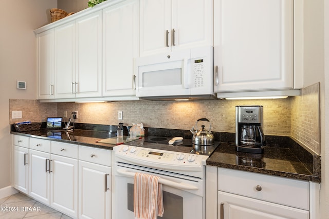 kitchen with tasteful backsplash, dark stone counters, light tile patterned floors, white cabinets, and white appliances