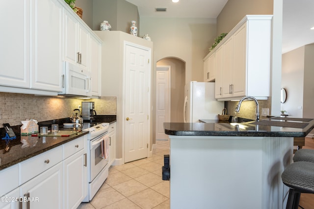 kitchen with white appliances, white cabinetry, light tile patterned floors, and kitchen peninsula