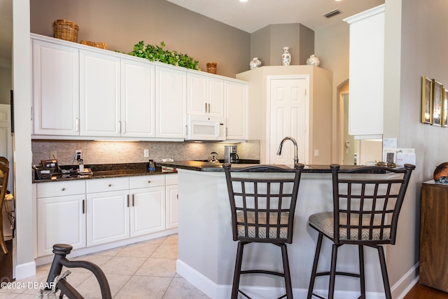 kitchen featuring backsplash, a kitchen bar, light tile patterned floors, white cabinets, and kitchen peninsula