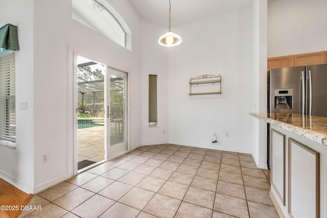 unfurnished dining area with light tile patterned floors, a towering ceiling, and a healthy amount of sunlight