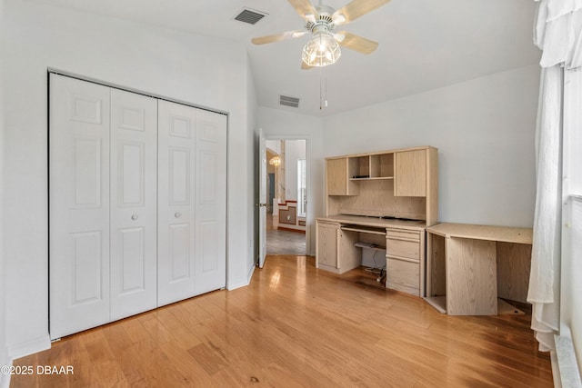 unfurnished office featuring vaulted ceiling, built in desk, ceiling fan, and light hardwood / wood-style floors