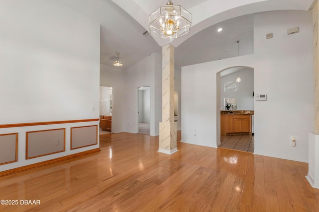 spare room with sink, a chandelier, high vaulted ceiling, and light wood-type flooring