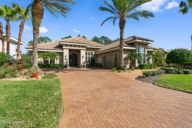 650 Woodbridge Dr, Ormond Beach, FL 32174 - mediterranean / spanish home with decorative driveway, an attached garage, a tile roof, stucco siding, and a front yard