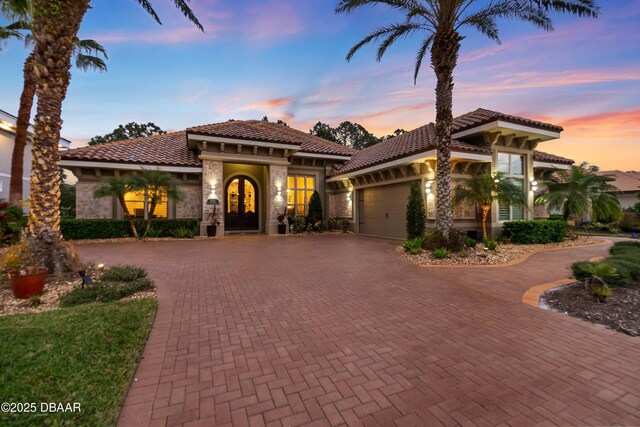 650 Woodbridge Dr, Ormond Beach, FL 32174 - mediterranean / spanish-style house with curved driveway, a garage, a tiled roof, stone siding, and stucco siding