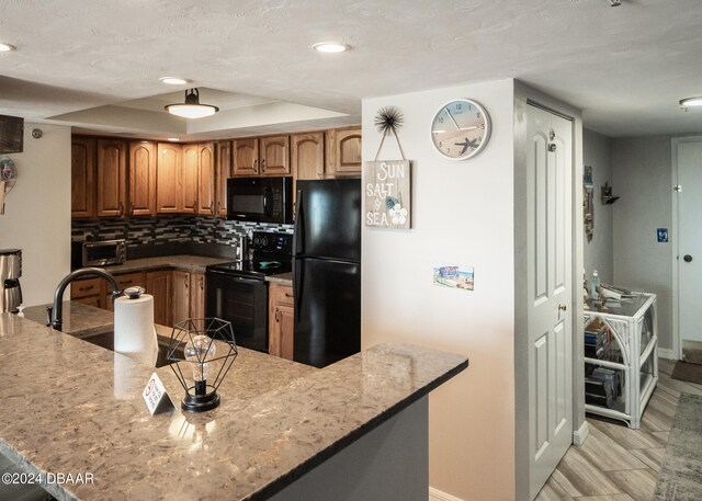 kitchen with decorative backsplash, kitchen peninsula, black appliances, a tray ceiling, and light stone countertops