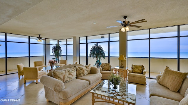 living room featuring ceiling fan, light tile patterned flooring, a wall of windows, and a water view