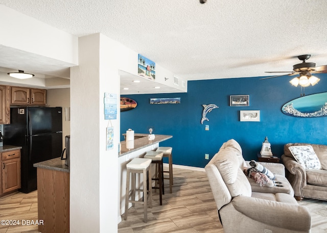 interior space with a kitchen bar, black fridge, a textured ceiling, ceiling fan, and light wood-type flooring