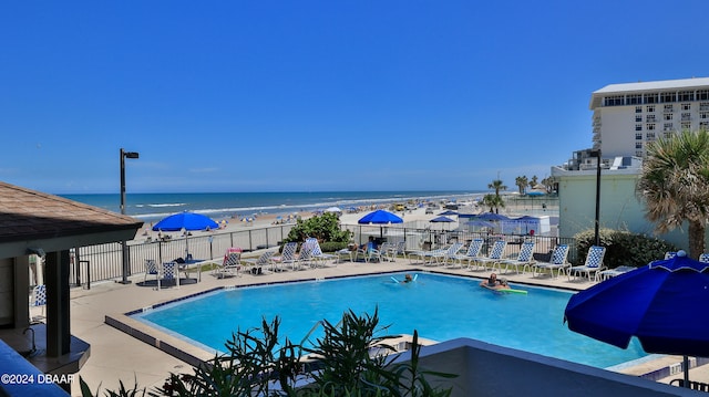 view of pool with a patio, a water view, a view of the beach, and area for grilling