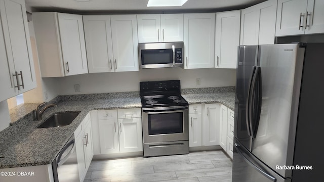 kitchen with stainless steel appliances, stone countertops, white cabinetry, and sink