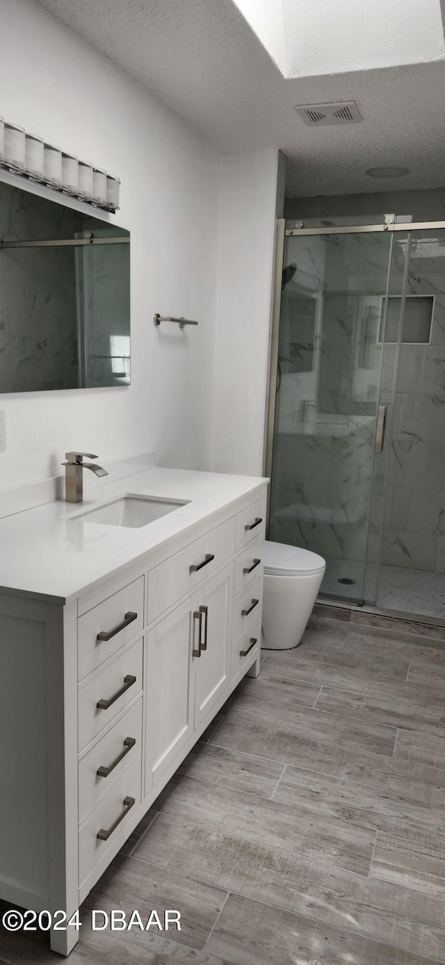 bathroom with vanity, a shower with shower door, a textured ceiling, and toilet