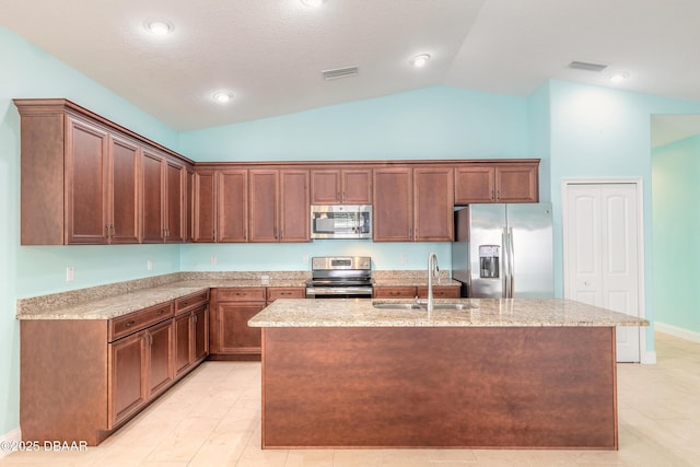 kitchen featuring an island with sink, appliances with stainless steel finishes, vaulted ceiling, light stone counters, and sink