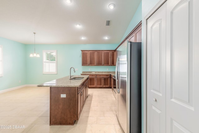 kitchen with decorative light fixtures, sink, a notable chandelier, stainless steel refrigerator, and light stone counters