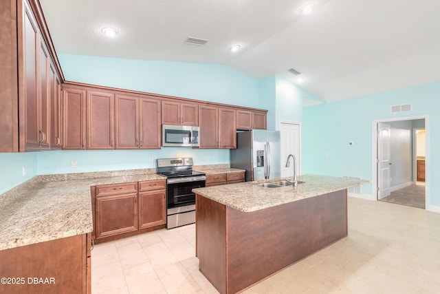 kitchen with light stone countertops, stainless steel appliances, sink, a kitchen island with sink, and vaulted ceiling