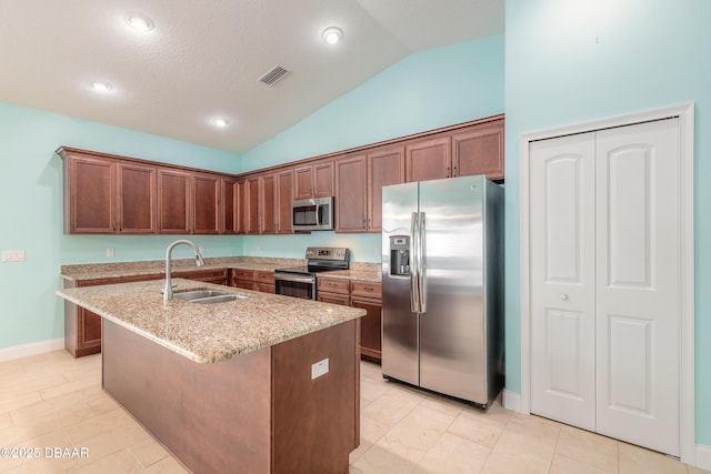 kitchen with vaulted ceiling, a center island with sink, sink, appliances with stainless steel finishes, and light stone counters