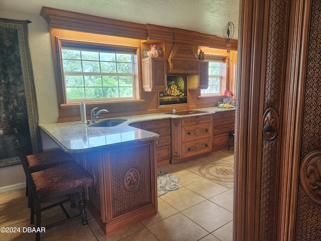 kitchen with black electric stovetop, light tile patterned floors, sink, a breakfast bar area, and kitchen peninsula