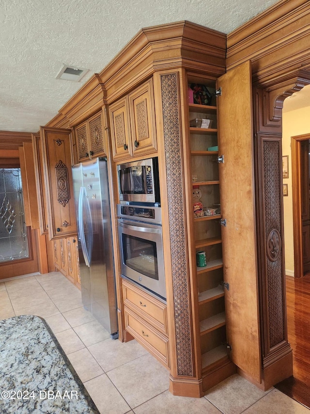 kitchen with a textured ceiling, light tile patterned flooring, and stainless steel appliances