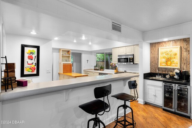 120 Beach St, Ponce Inlet, FL 32127 - kitchen featuring stainless steel microwave, beverage cooler, a breakfast bar, light wood finished floors, and a peninsula