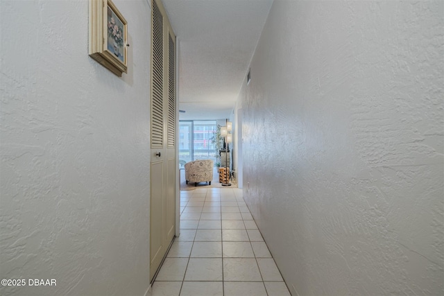 corridor with light tile patterned floors, a textured wall, and visible vents