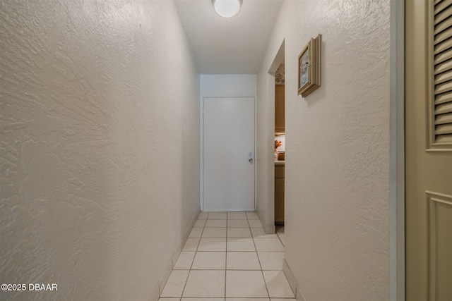 hall with a textured wall, a textured ceiling, and light tile patterned floors