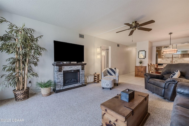 carpeted living area featuring ceiling fan, a fireplace, visible vents, and a textured ceiling